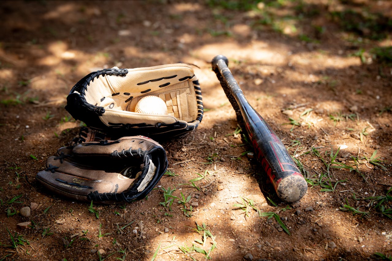 Baseball glove, bat, and ball on a dusty outdoor field, perfectly capturing the sport's essence.