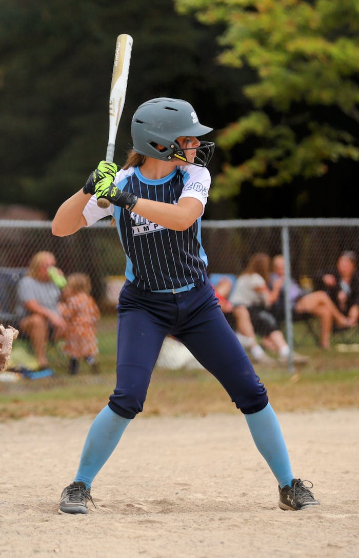 A determined softball player in full uniform prepares to bat on an outdoor field.