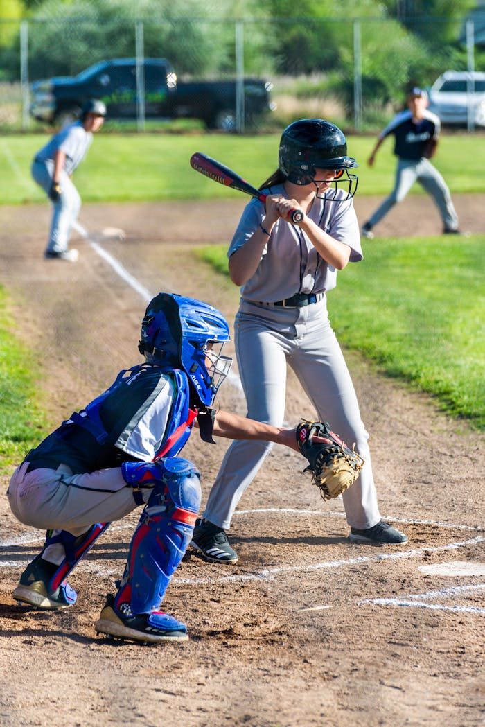 Kids playing baseball, batter ready to hit while catcher and pitcher prepare during a sunny game day.