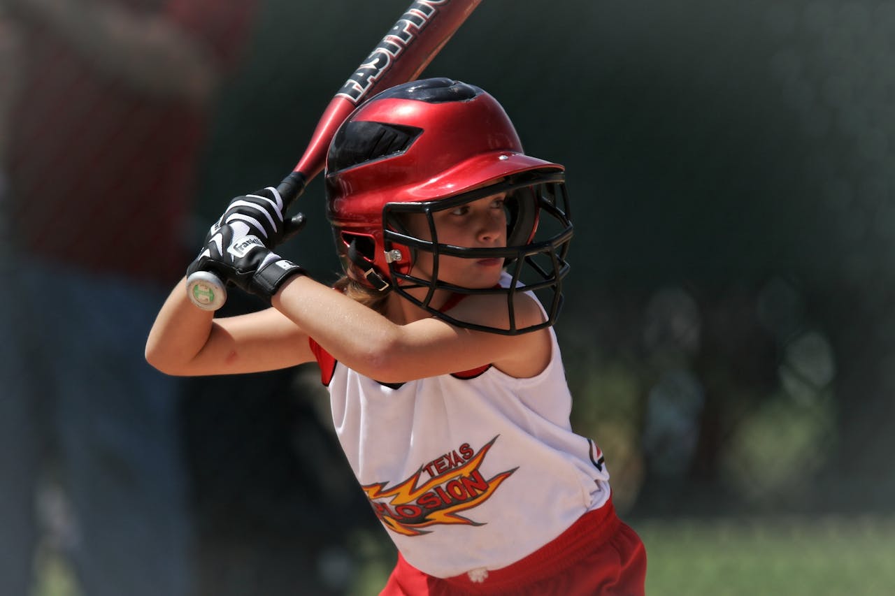 Young girl concentrating on batting during an outdoor baseball game.
